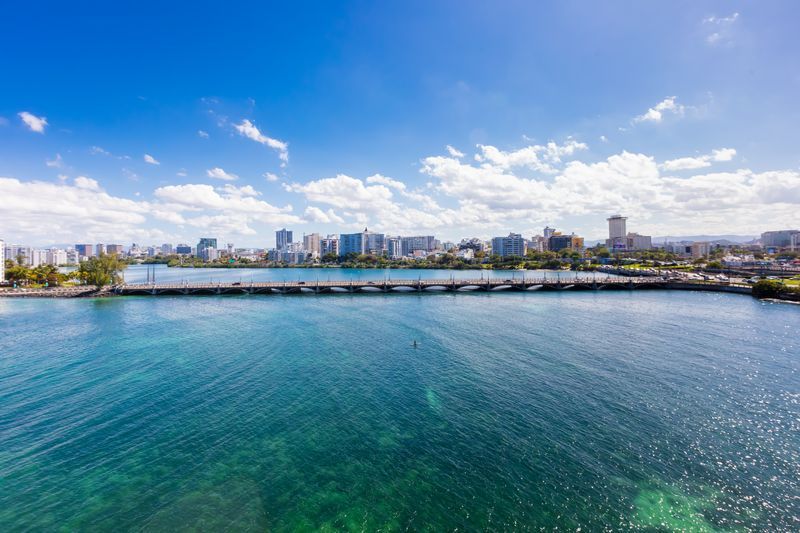 City skyline across a calm blue bay under a bright sky with scattered clouds