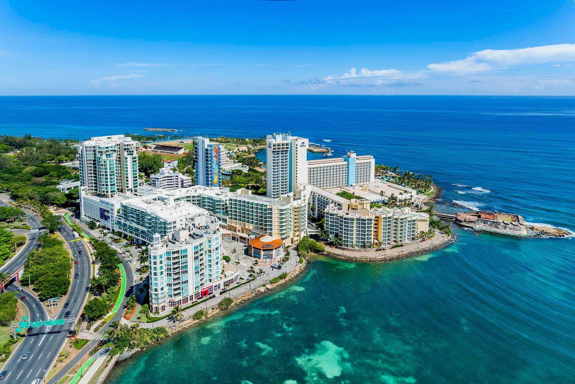 Aerial view of a seaside resort with high-rise condos beside turquoise ocean and a curving shoreline