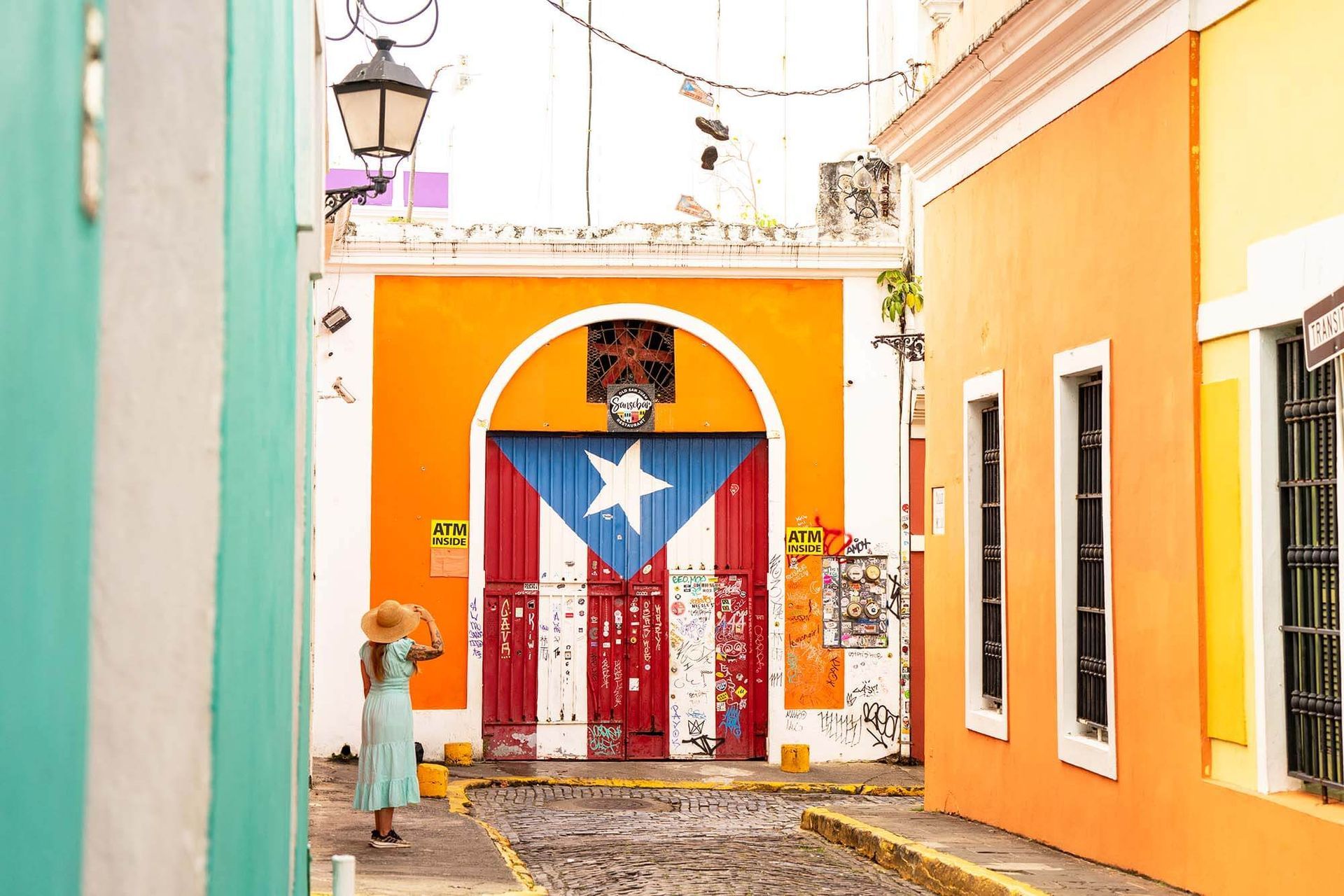Colorful narrow street with bright orange walls and a Puerto Rican flag mural on a gated door
