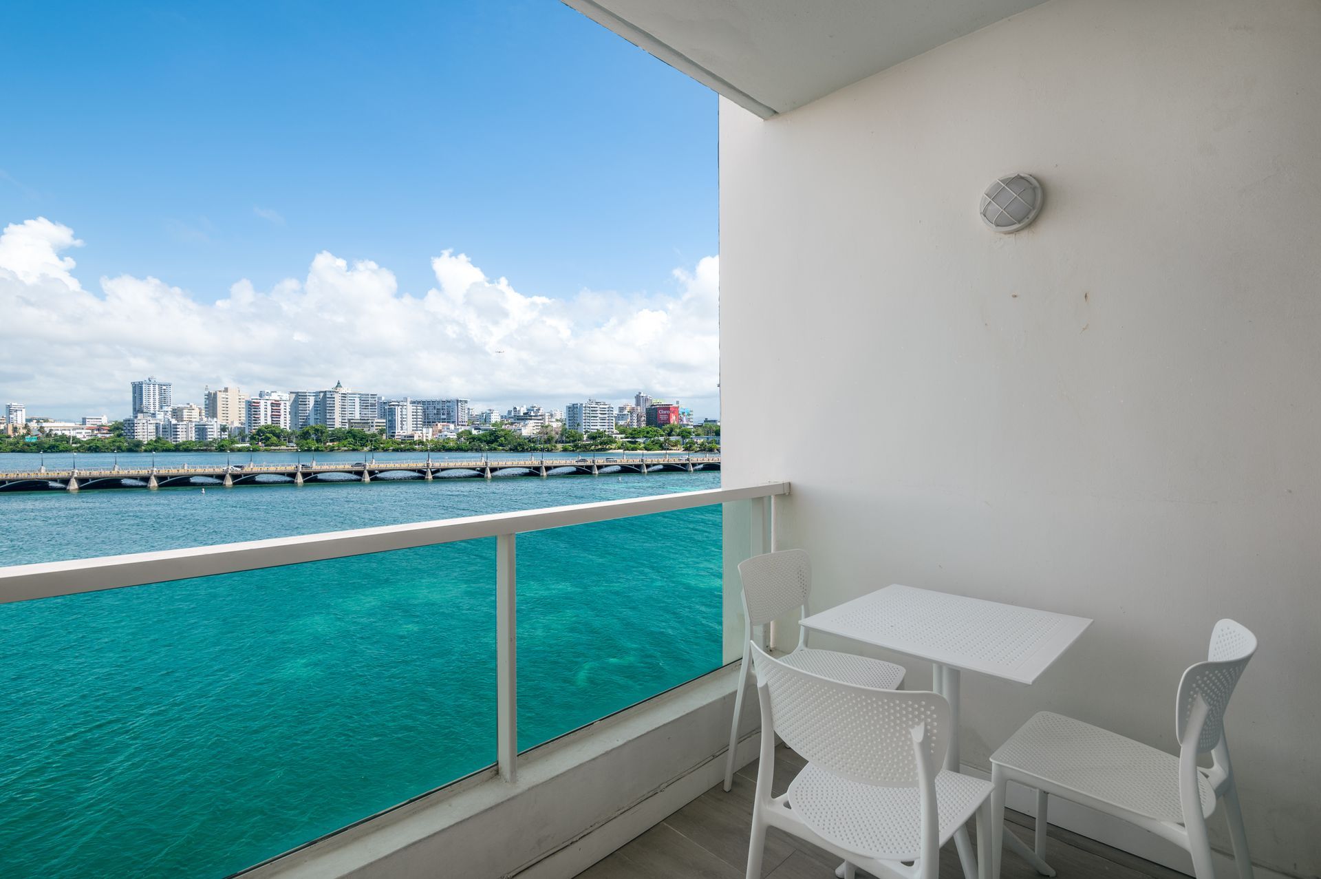 Balcony with white table and chairs overlooking turquoise water and a distant city skyline