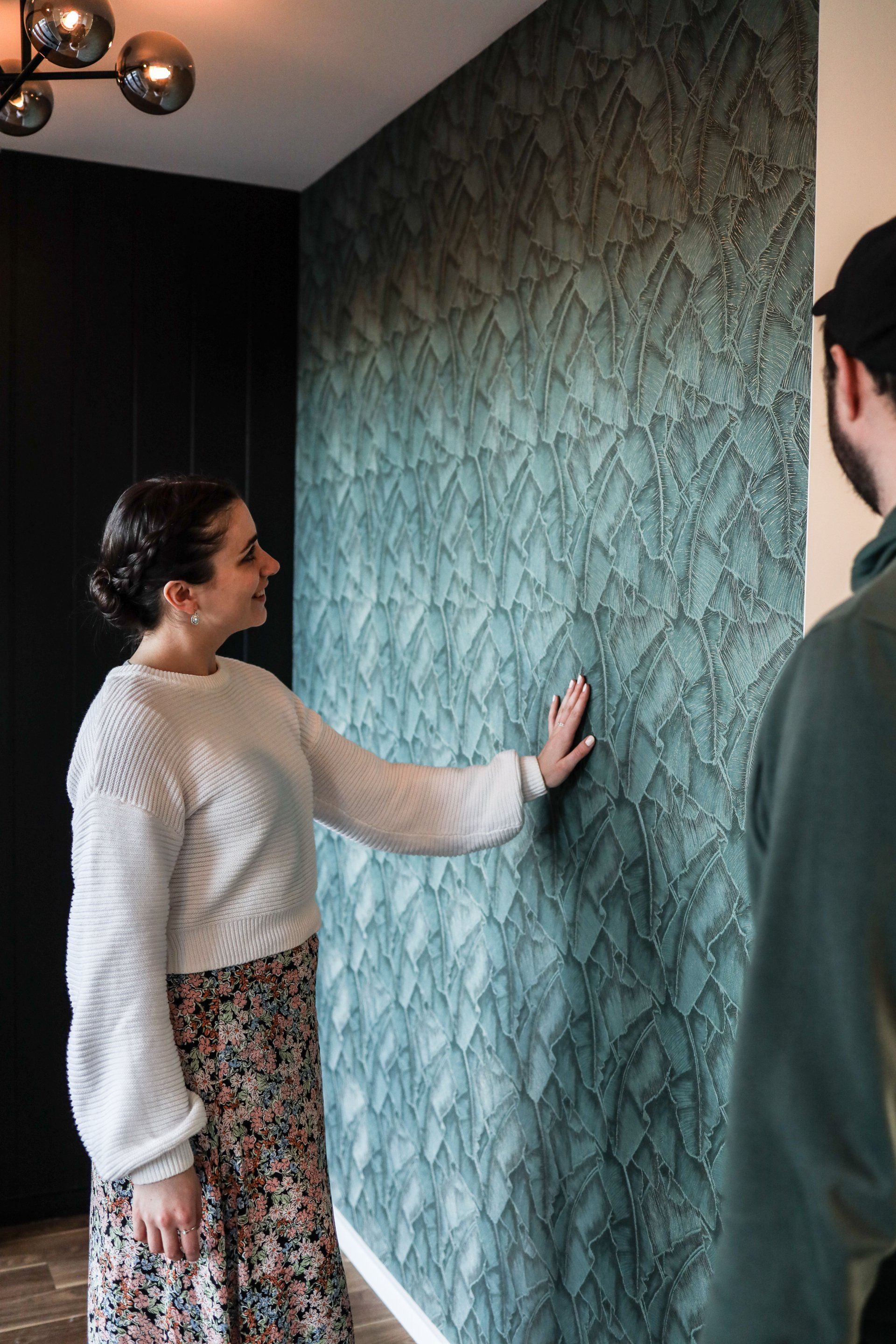 A woman is touching a wall while a man looks on.