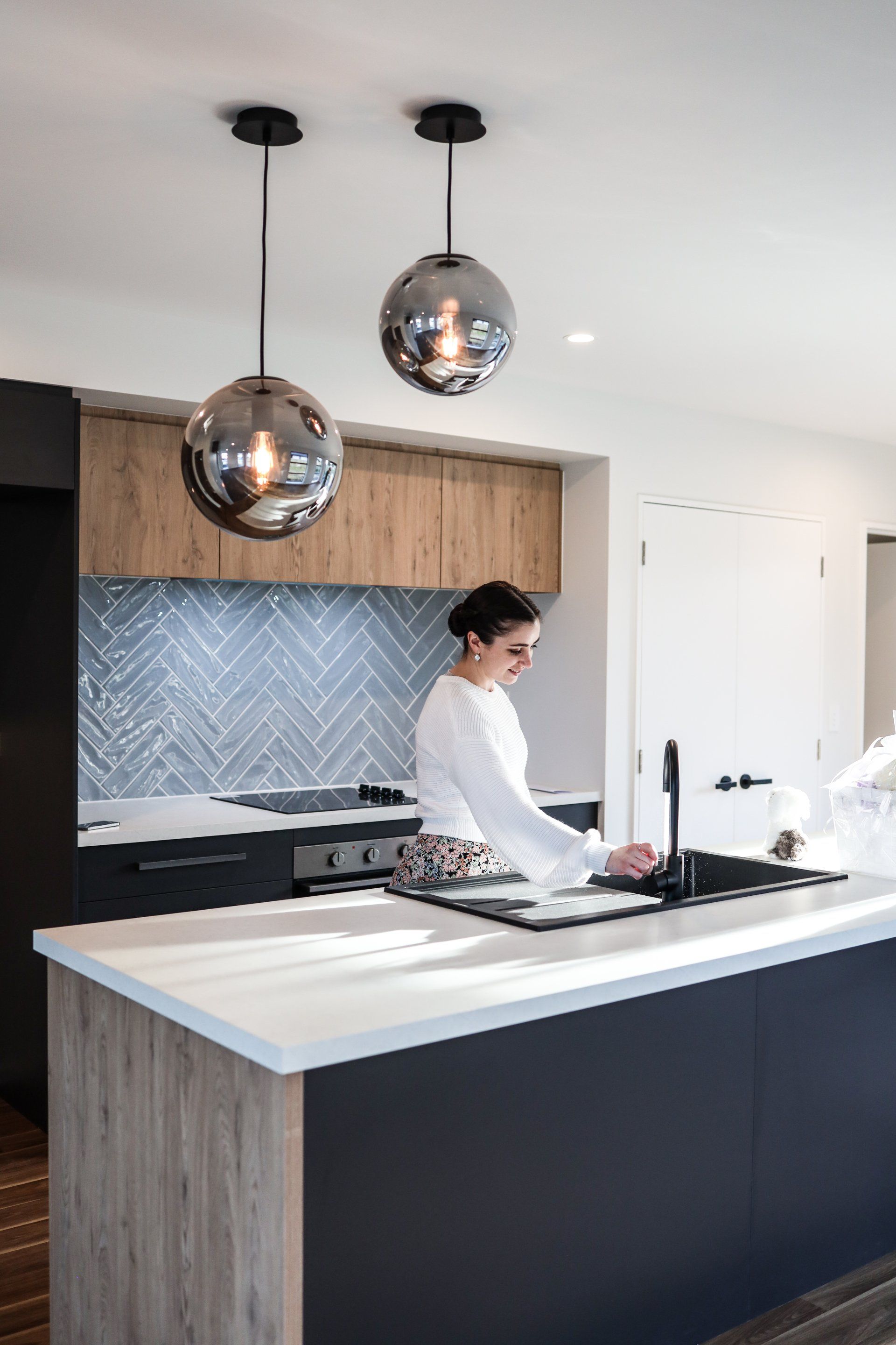 A woman is standing in a kitchen at a sink.