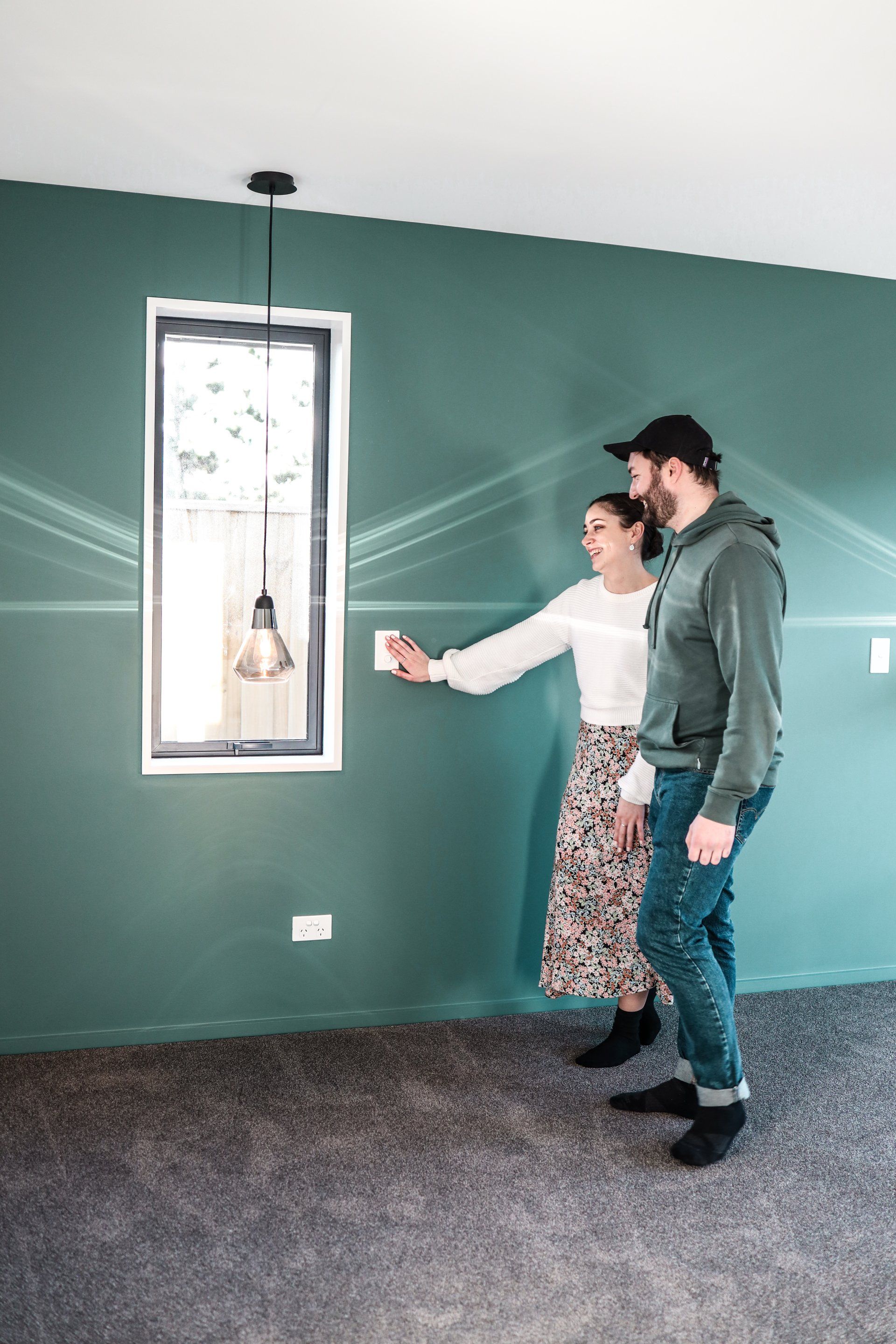A man and a woman are standing in an empty room looking at a picture on the wall.