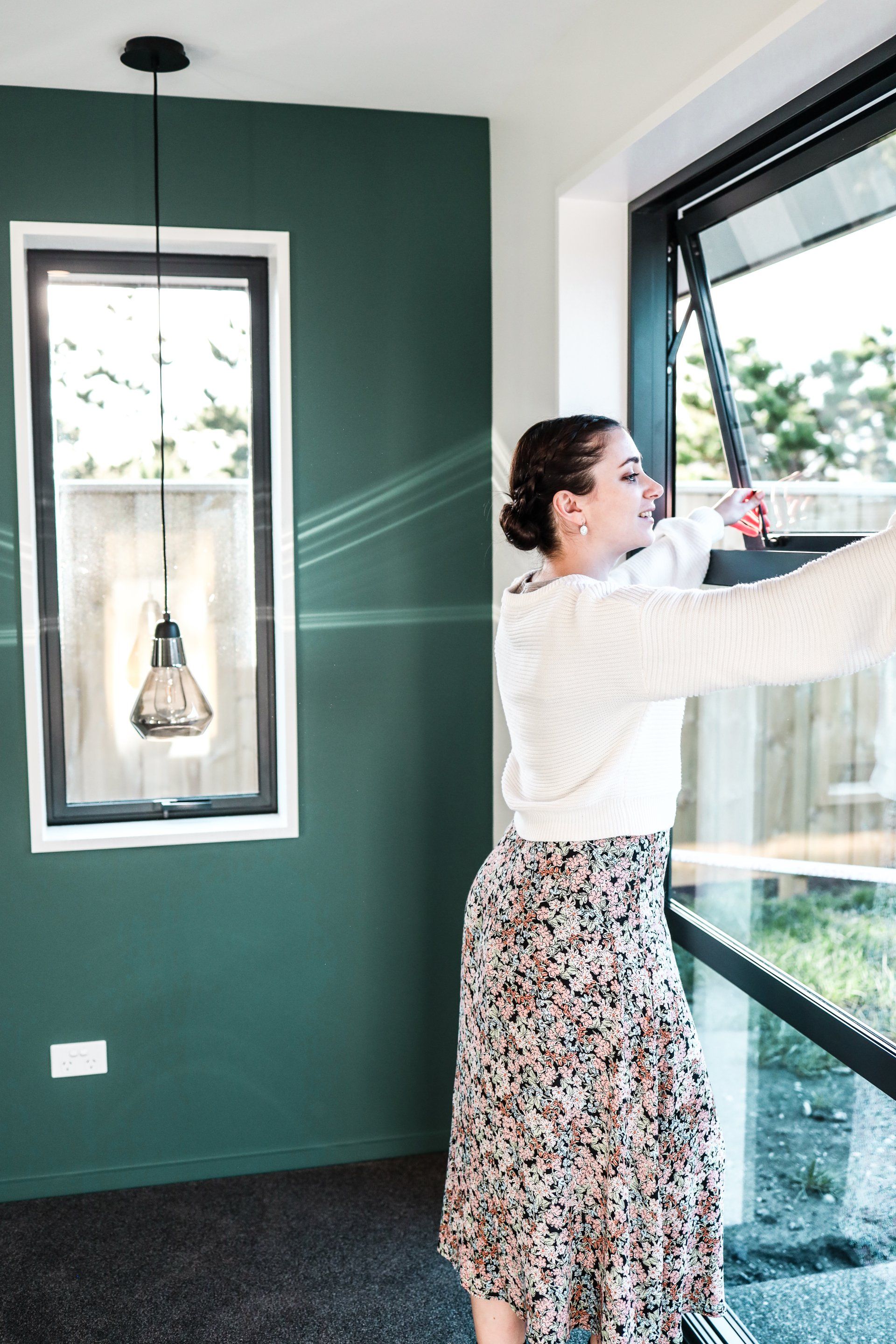 A woman is cleaning a window in a room with a green wall.