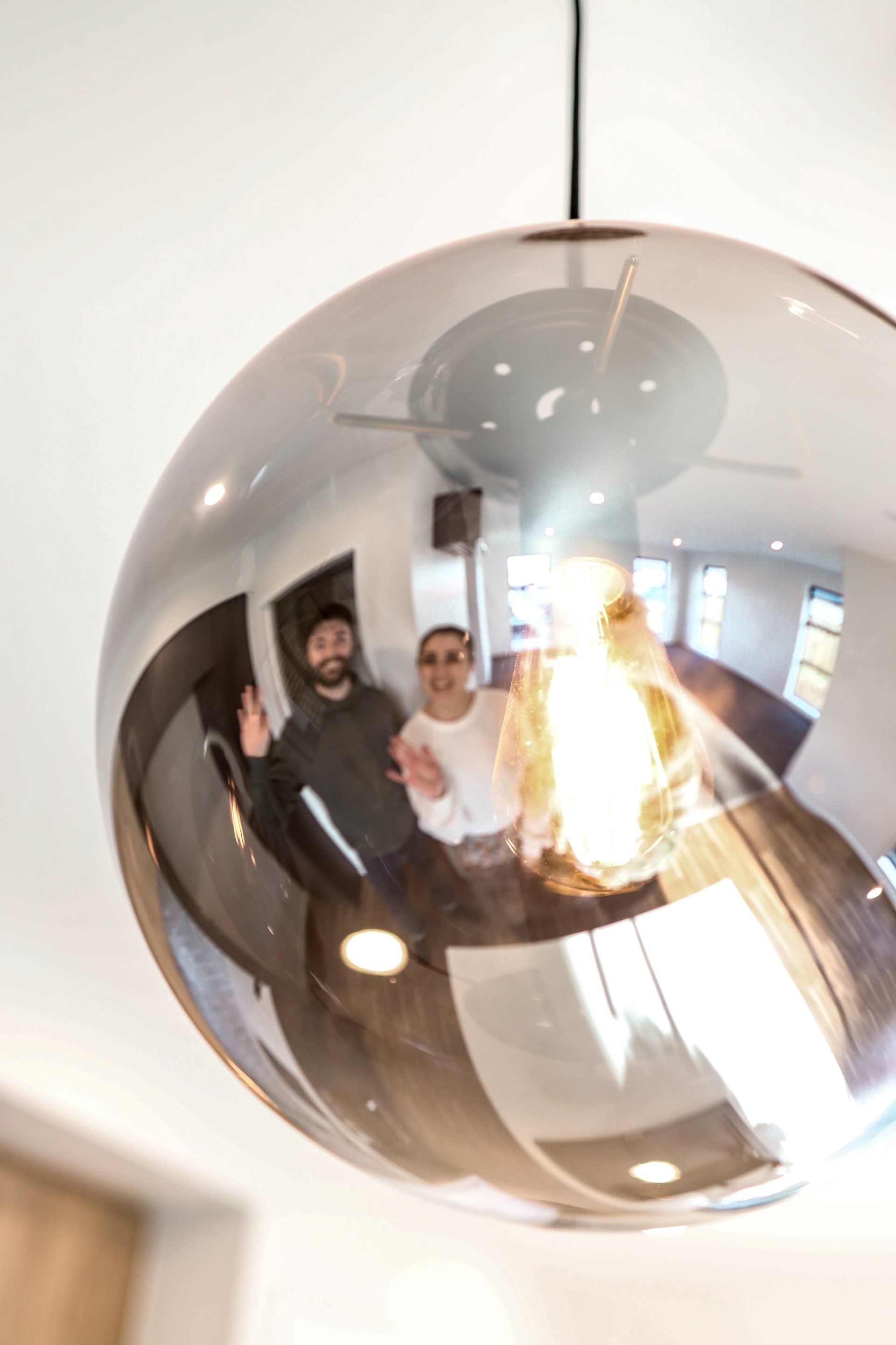 Two men are standing in front of a mirror hanging from the ceiling.
