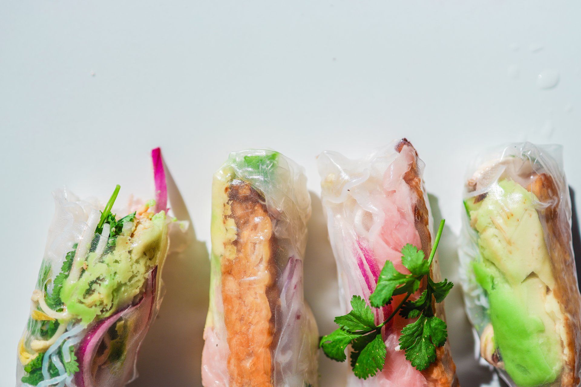A row of spring rolls with different toppings on a white plate.