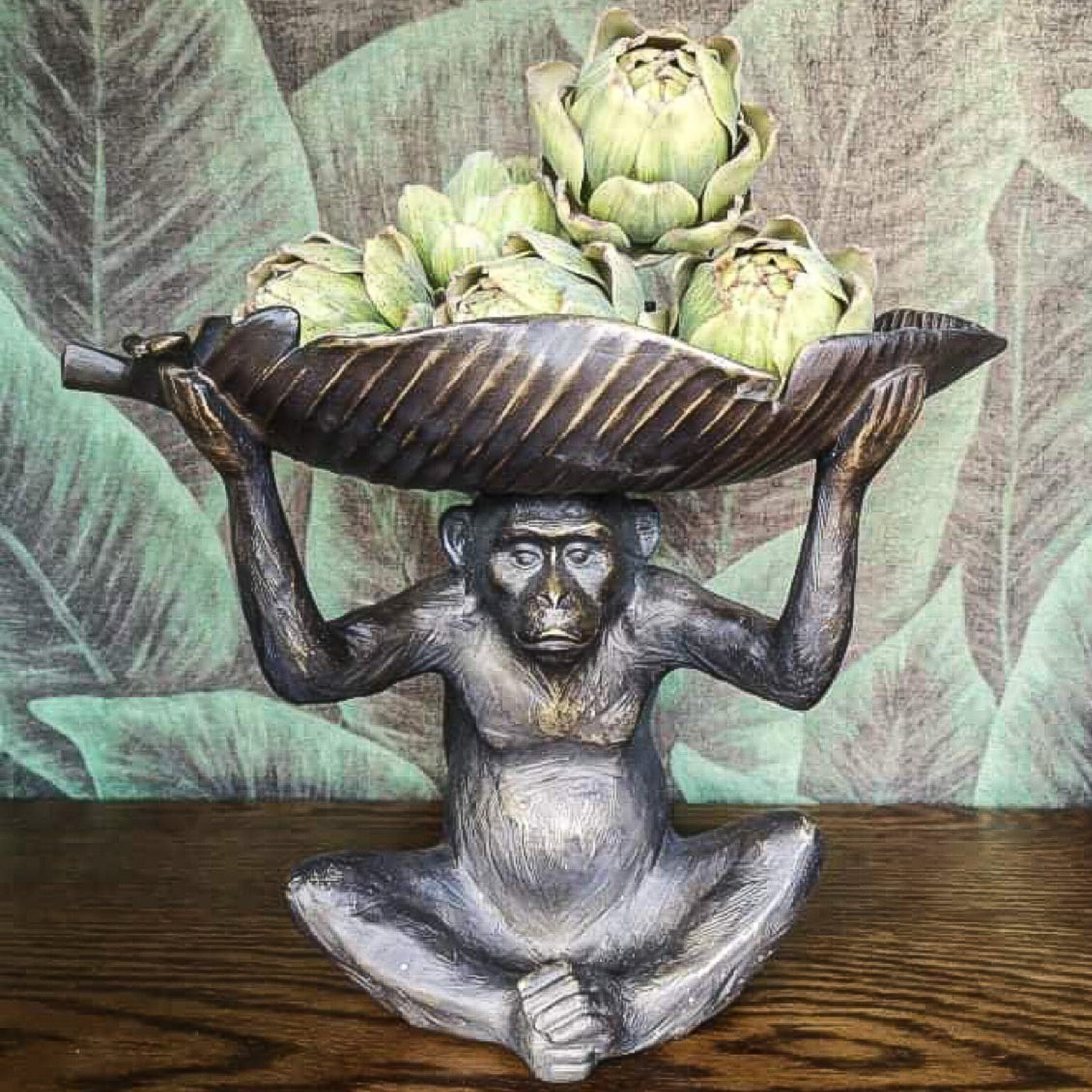 A statue of a monkey holding a bowl of artichokes on its head.