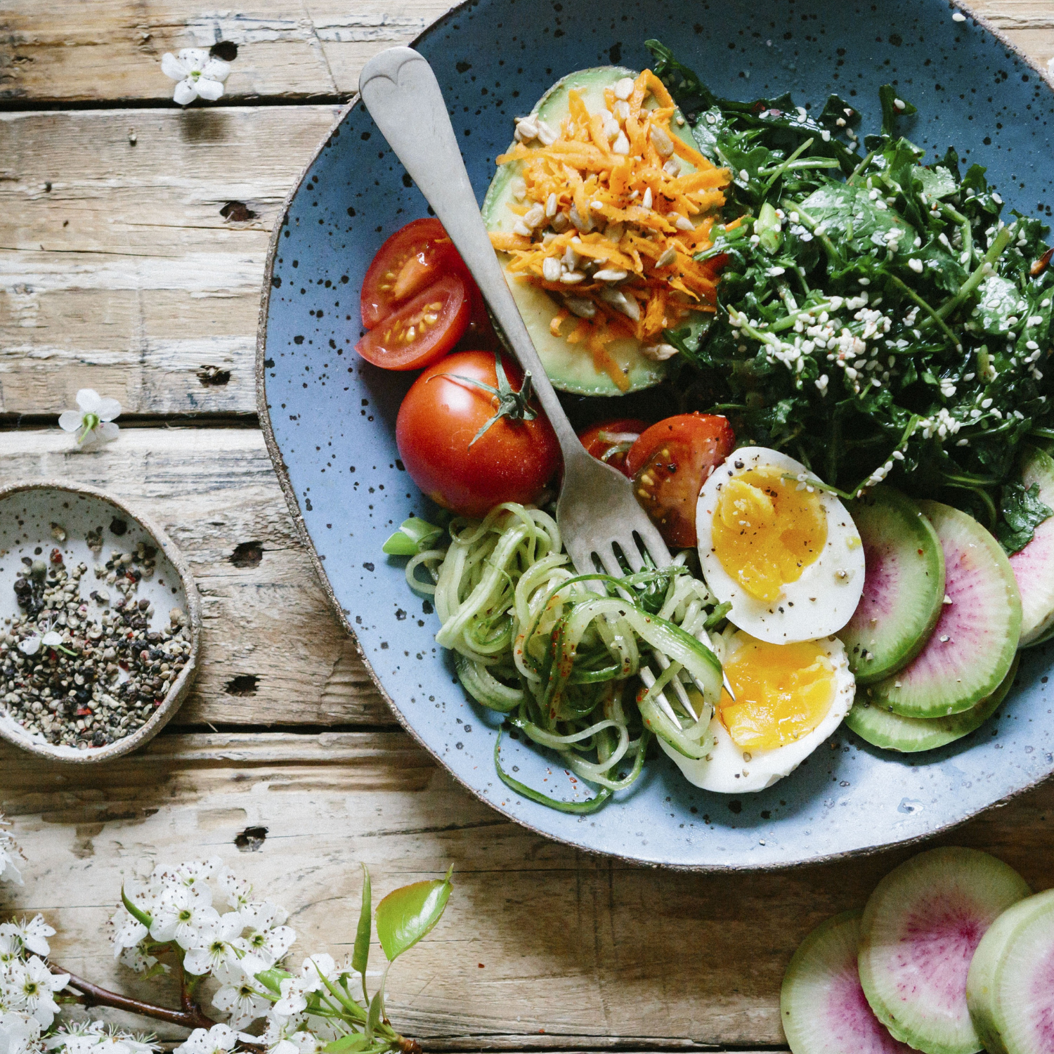 A blue bowl filled with vegetables and eggs on a wooden table.