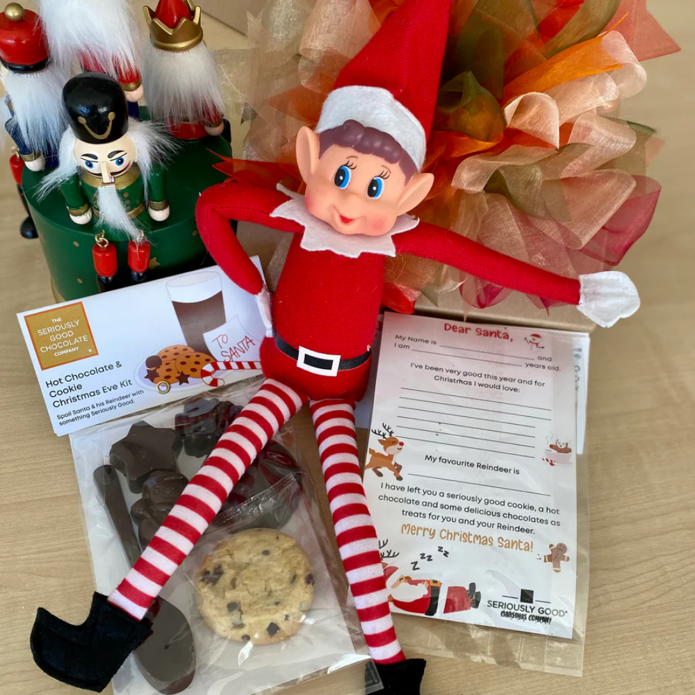 An elf on the shelf is sitting next to a bag of cookies and a nutcracker.