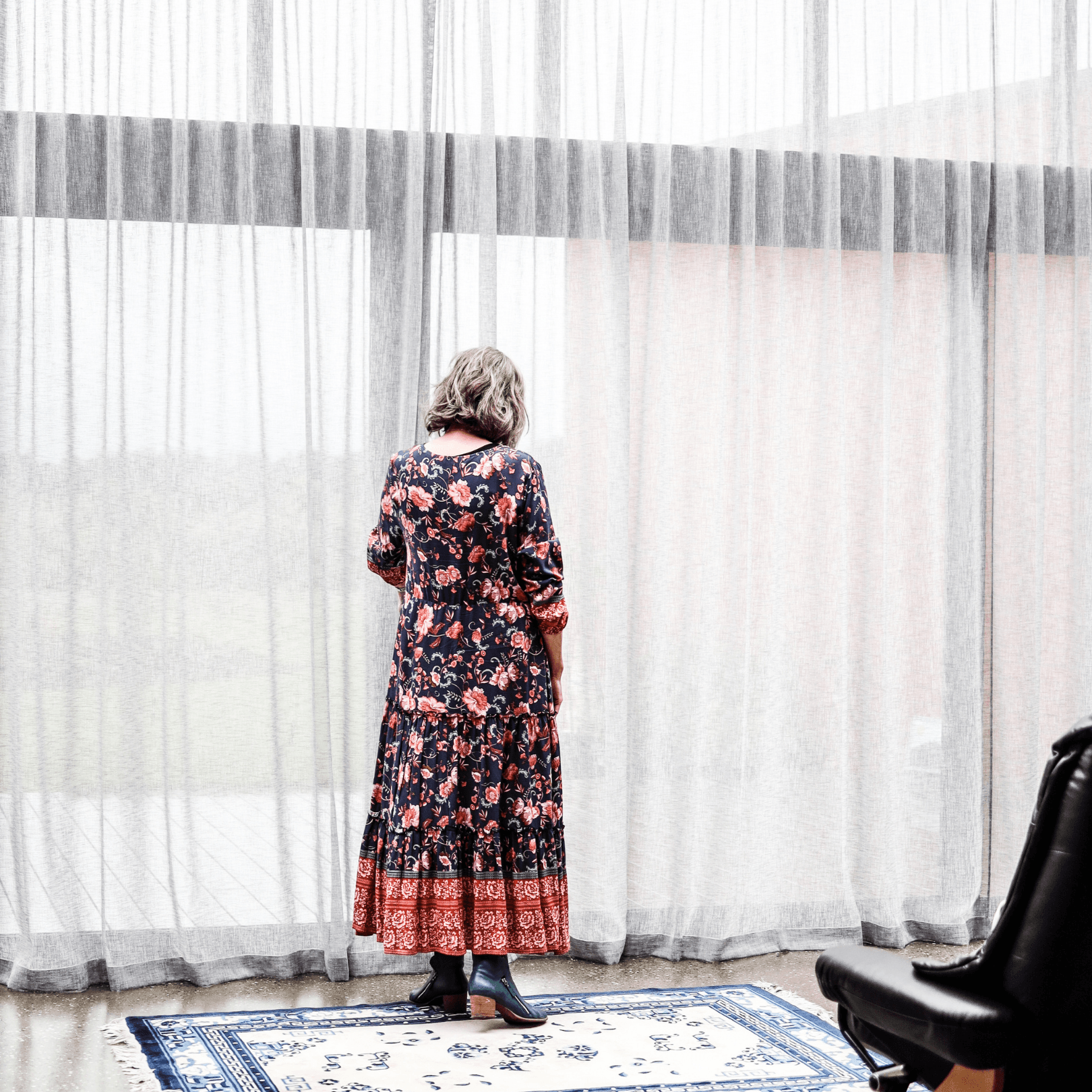 A woman in a dress is standing in front of a window.