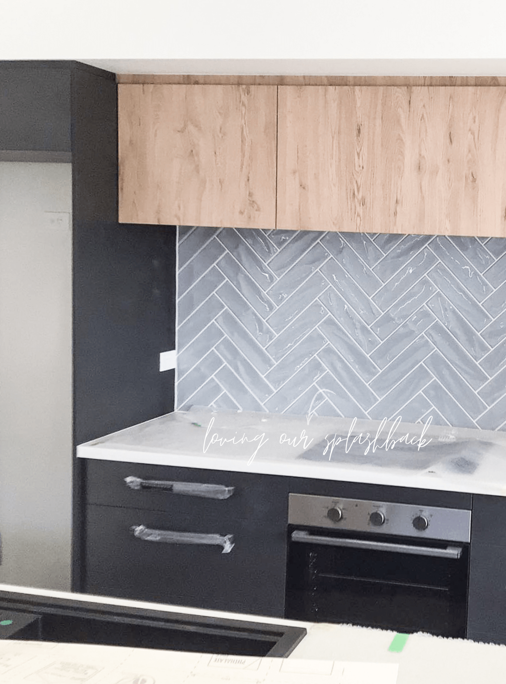 A kitchen with black cabinets , a stove , a sink , and a herringbone tile wall.