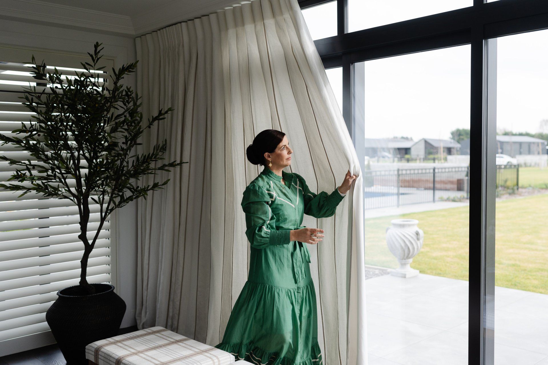 A woman in a green dress is standing in front of a large window.