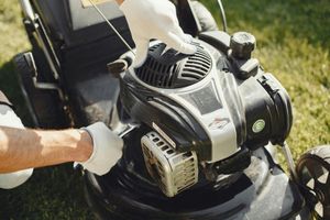 Person’s gloved hands adjusting a lawn mower engine outdoors