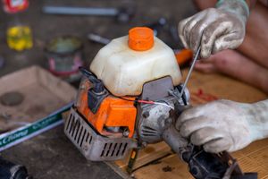 Hands repairing an orange and white chainsaw on a workbench