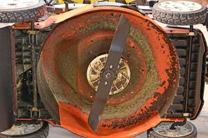 Overturned orange lawn mower with its blade and deck exposed, viewed from above