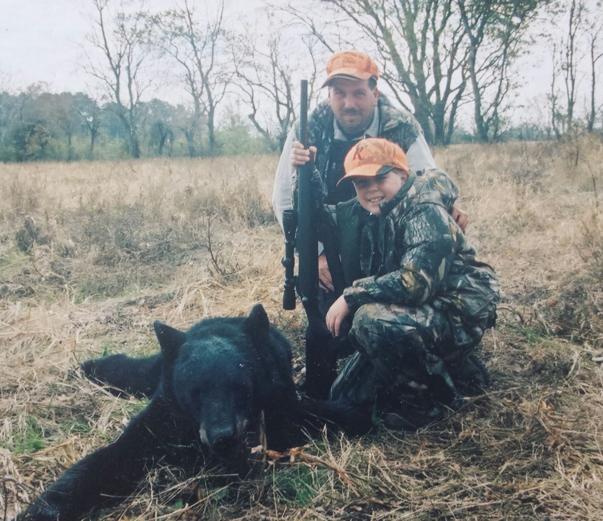 Two camouflaged hunters pose with a black boar in a dry field