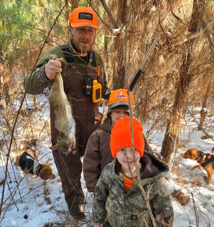 People in orange hats posing with hunted birds in a snowy wooded area