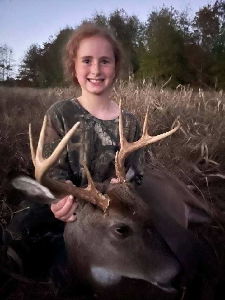 Smiling child holding a deer by the antlers in a grassy field at dusk