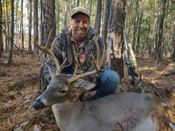 Hunter kneeling beside a large buck in a wooded forest