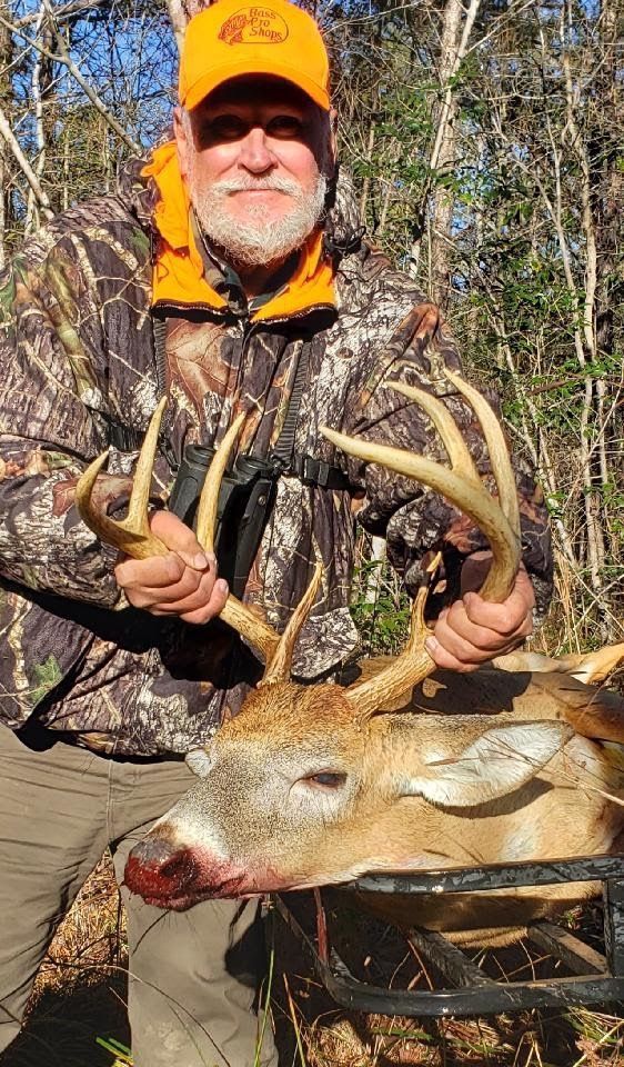 Hunter in camouflage holding a deer with large antlers in a wooded area