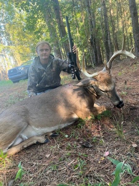 Hunter kneels beside a large antlered deer in a wooded area after a hunt