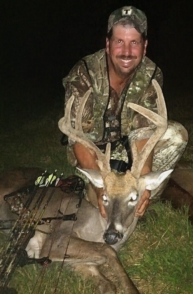 Hunter kneeling at night with a large deer he has just shot, holding the antlers.