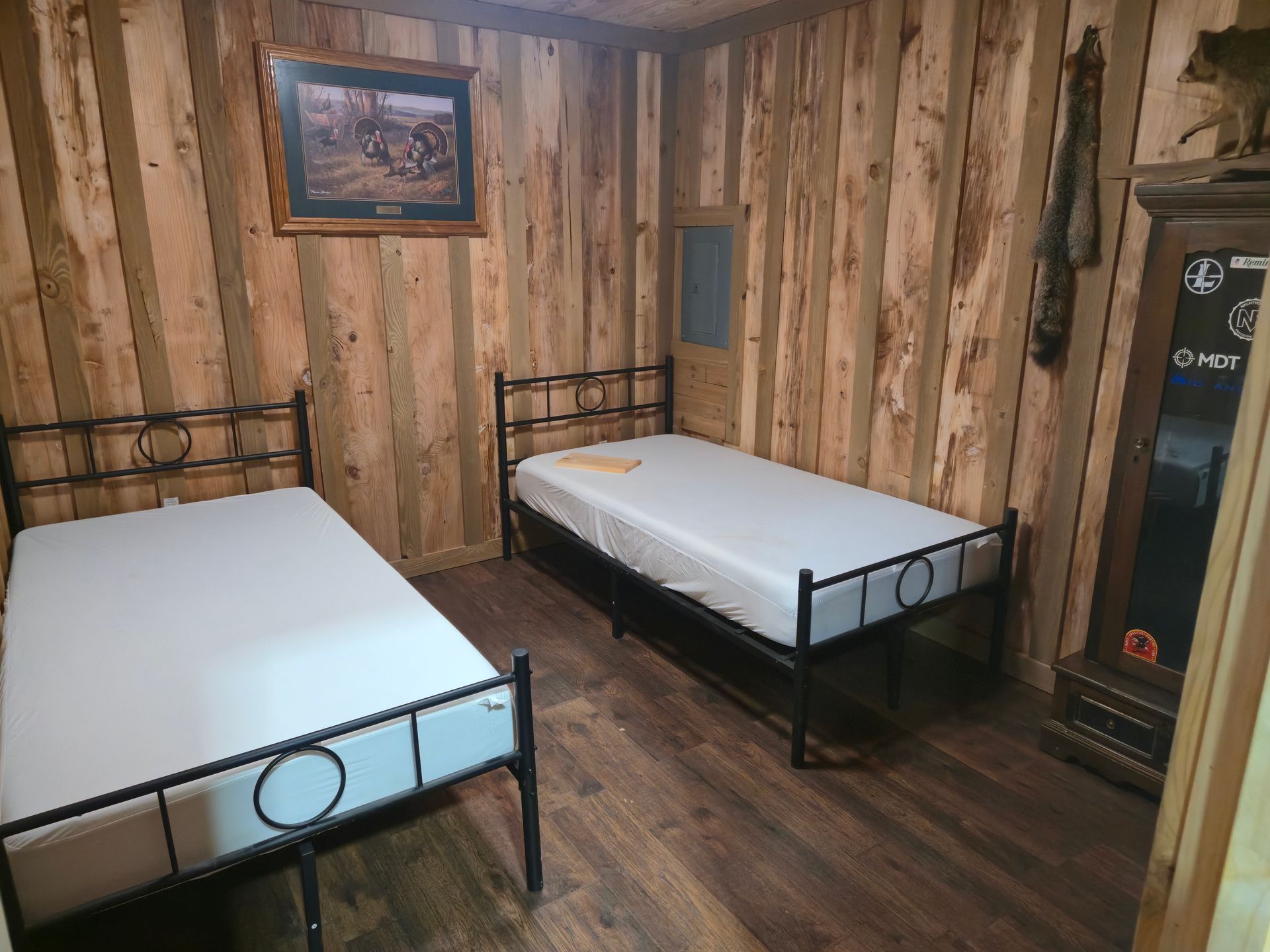 Rustic bedroom with two single beds, wood-paneled walls, and a framed picture above them