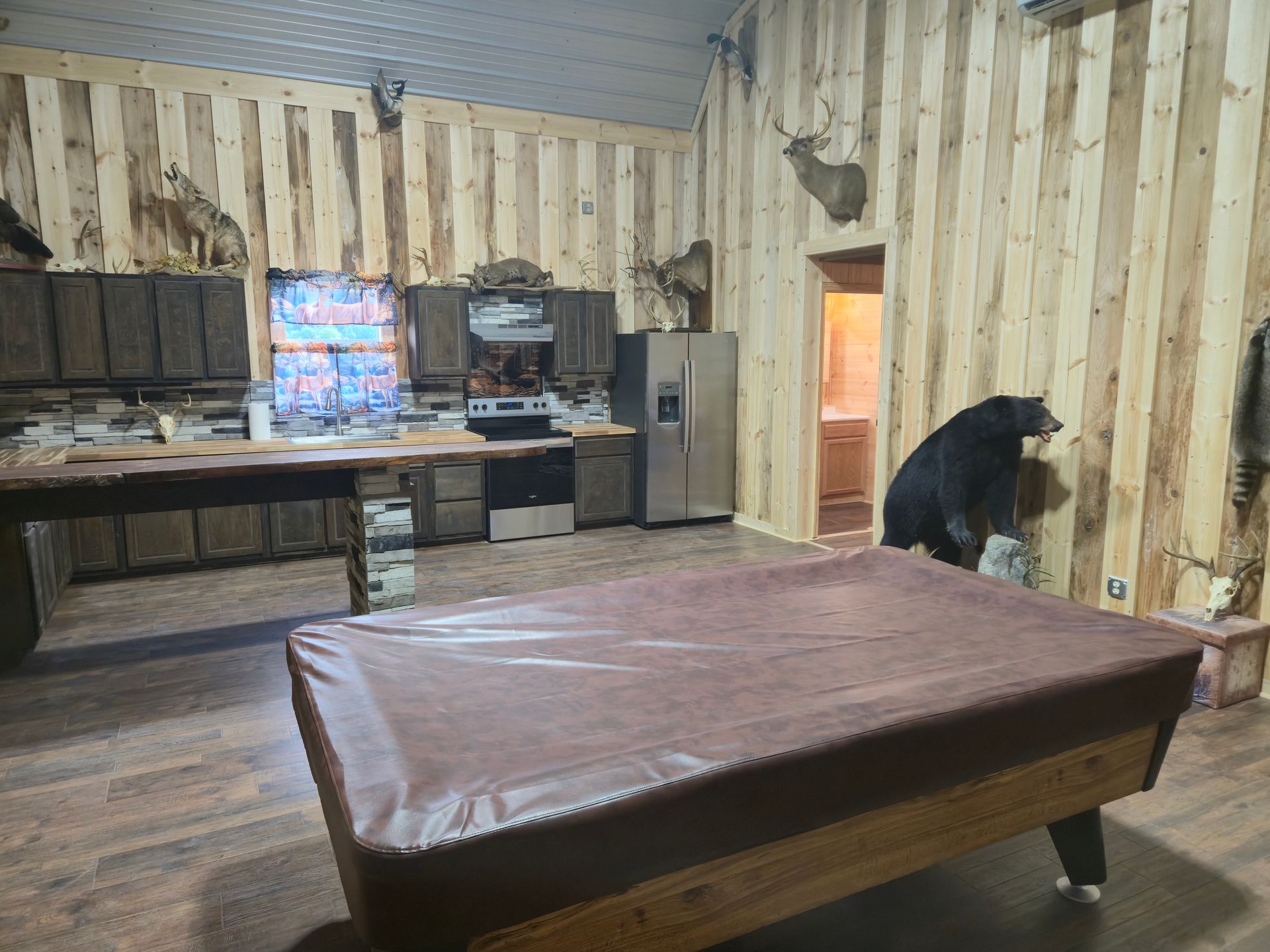 Rustic kitchen with wood-paneled walls, a large table, and a person near the doorway.