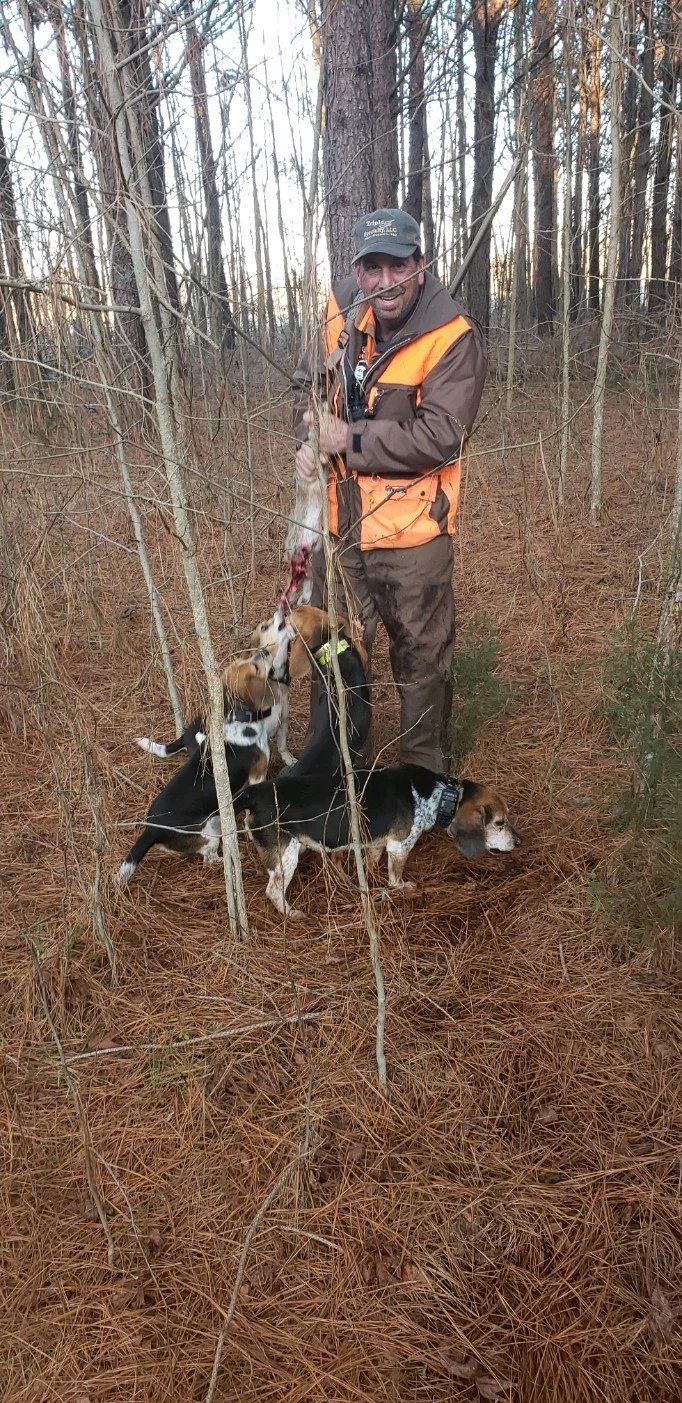 Hunter in orange vest holding a shotgun beside a black-and-white dog in a leafless woods