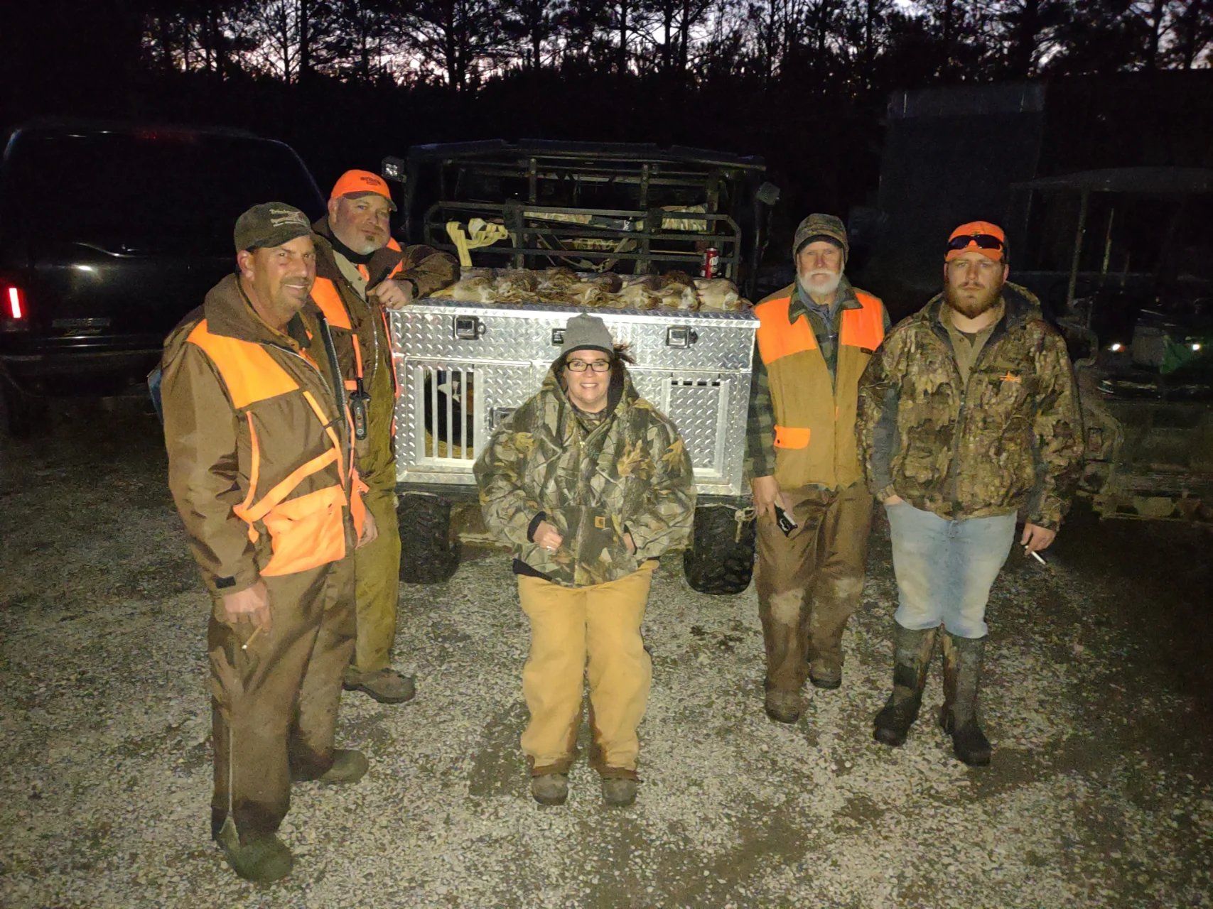 Five people in hunting gear standing in front of a truck at night outdoors.