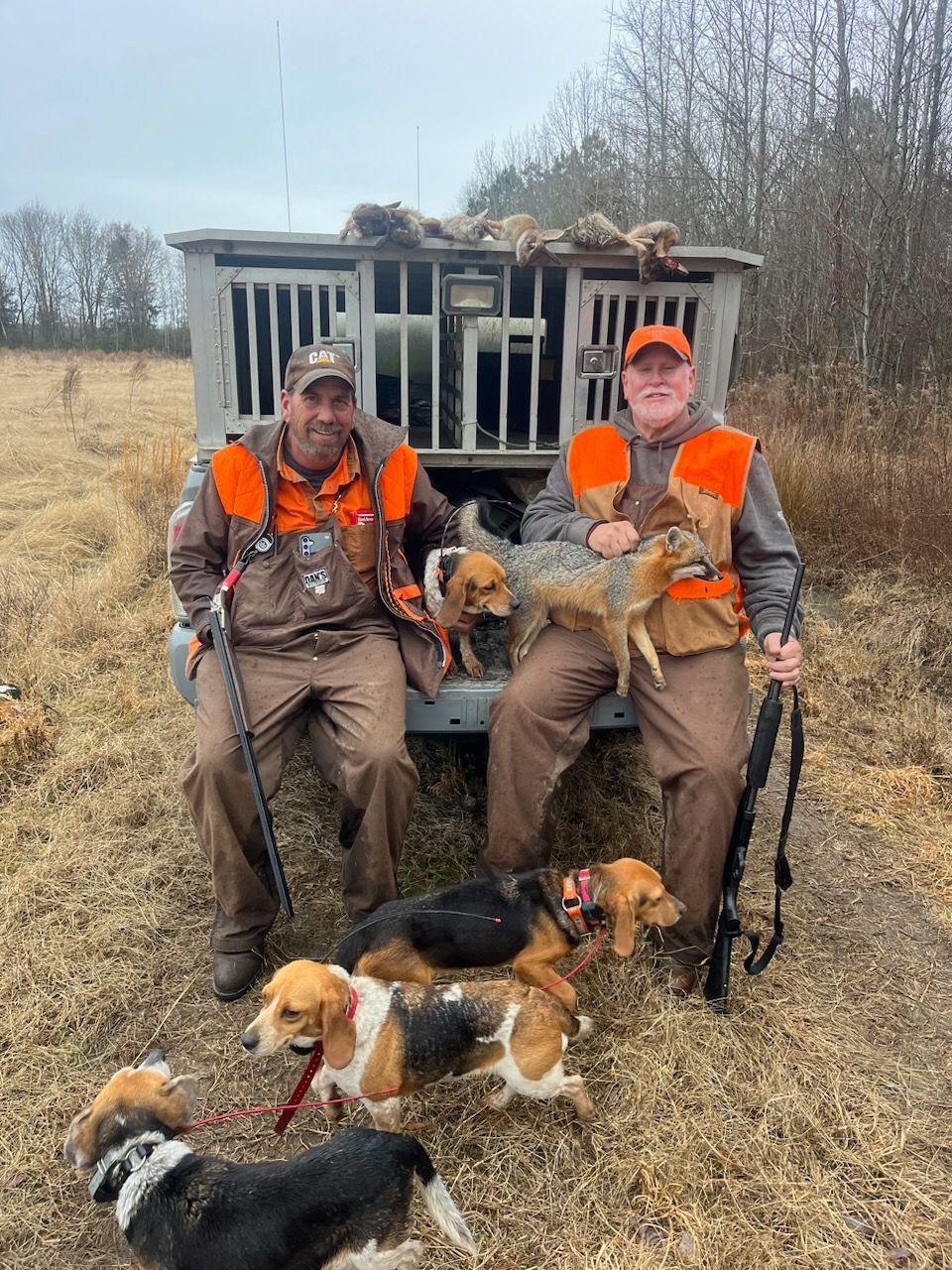Two hunters in blaze orange pose with five dogs in a field beside a hunting blind.
