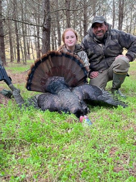 Hunters kneel beside a large turkey in a forest clearing during autumn.