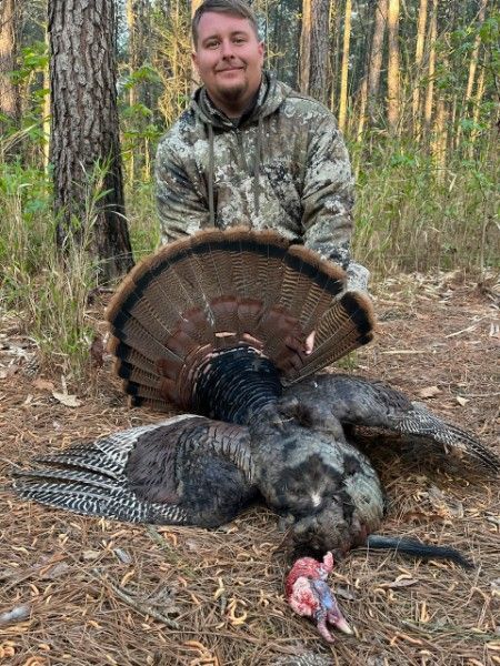 Man in camouflage holding a wild turkey in a wooded forest setting