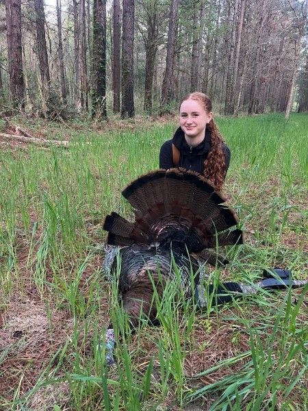 Person kneeling beside a wild turkey in a grassy forest clearing