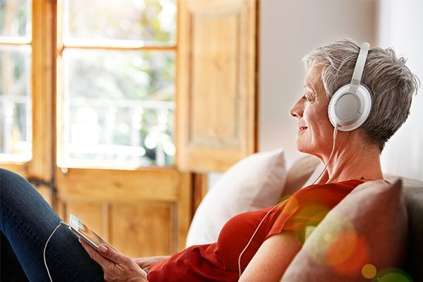 an elderly woman is sitting on a couch listening to music with headphones .