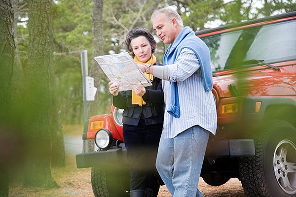 a man and a woman are standing next to a jeep looking at a map .