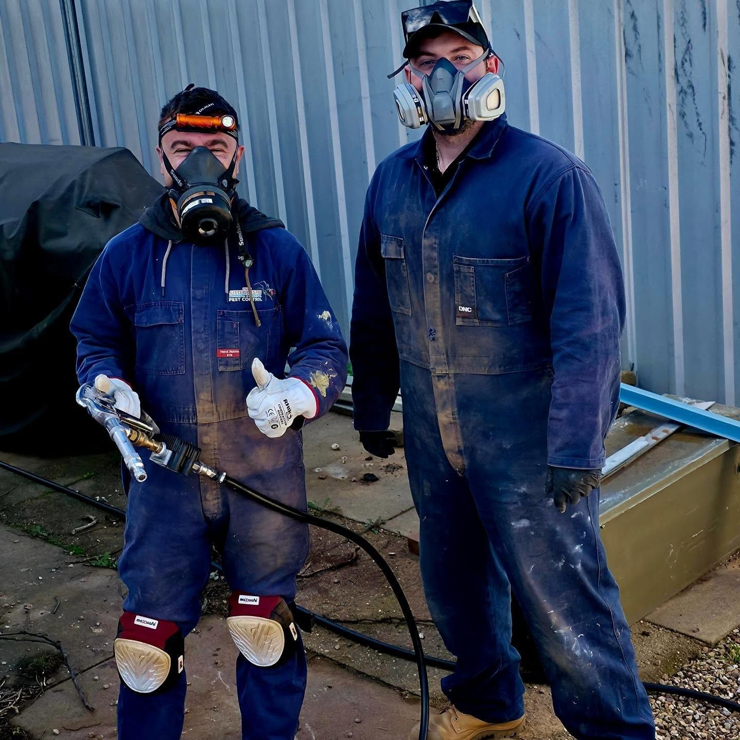 Two Pest Exterminators in Blue Overalls and Respirators Holding a Spray Hose and Tool — Pestie Bestie Pest Control In Shepparton, VIC