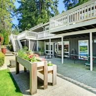 A multi-level suburban home with a large wooden planter in the foreground on a concrete patio.