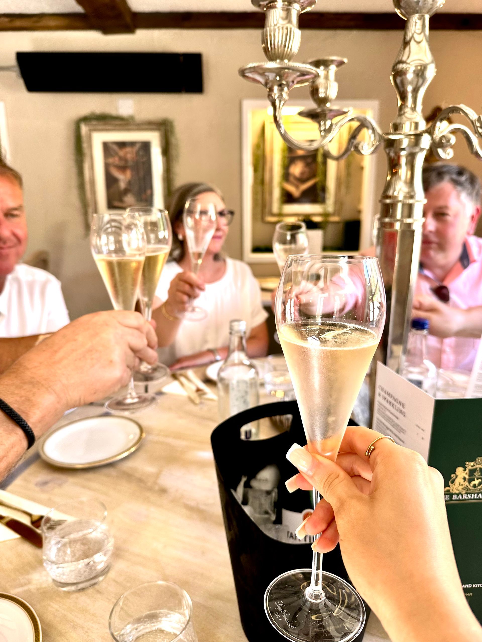 People toasting with champagne glasses at a restaurant table with a dessert tray