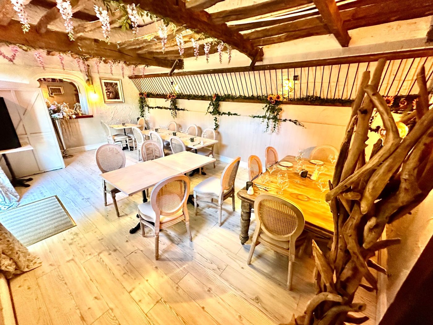 Rustic dining room with wooden tables, chairs, white tablecloths, and exposed beams.
