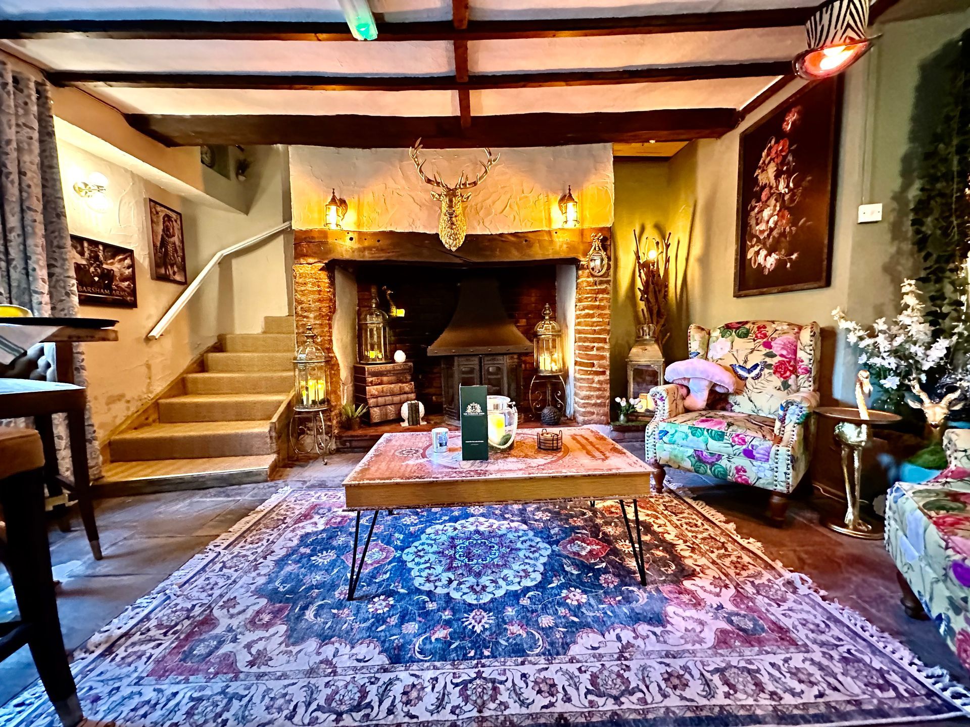 Cozy living room with a fireplace, staircase, patterned rug, and floral armchairs