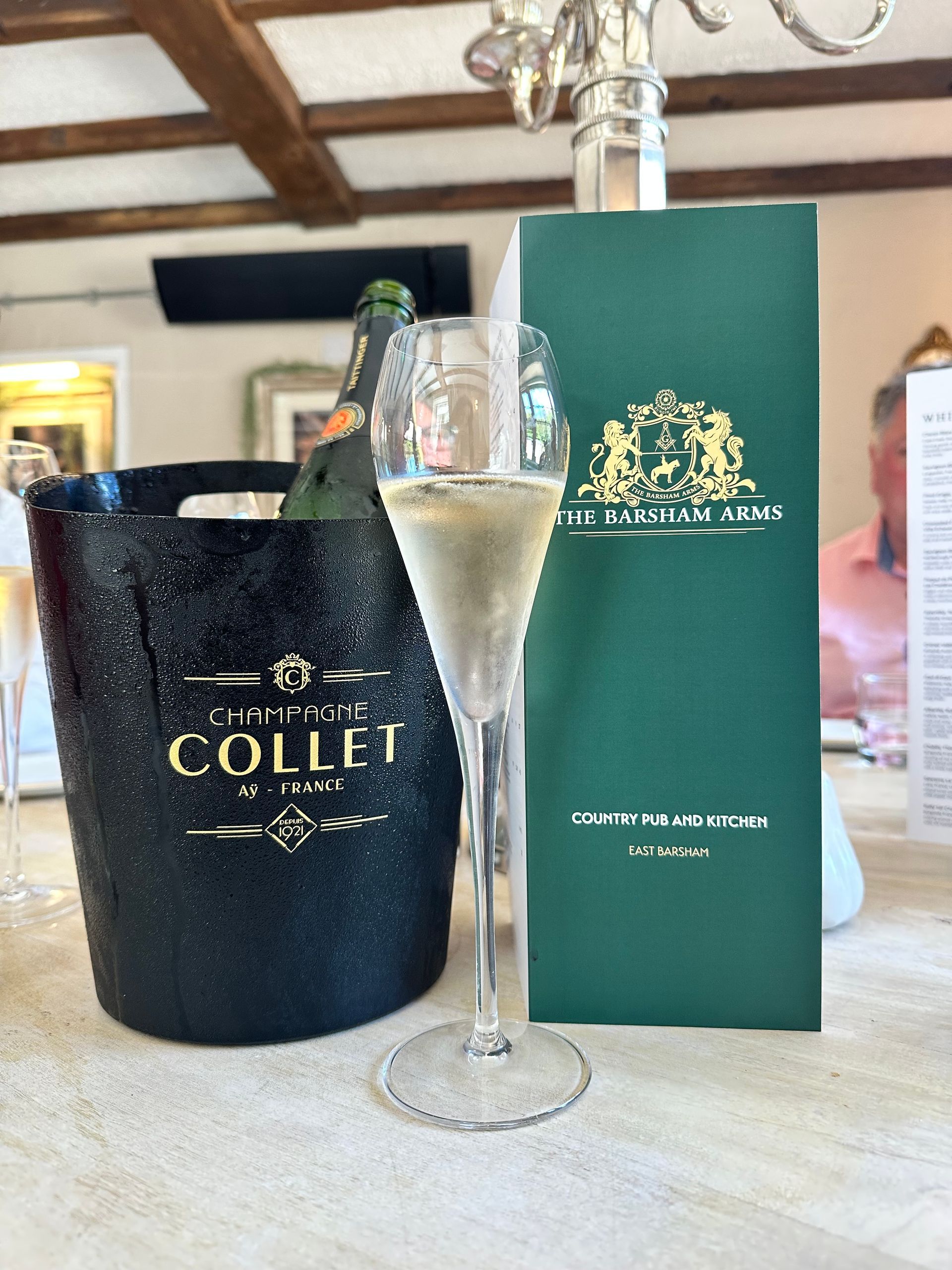 Sparkling wine bottle in a black COLET ice bucket beside a green gift bag on a table