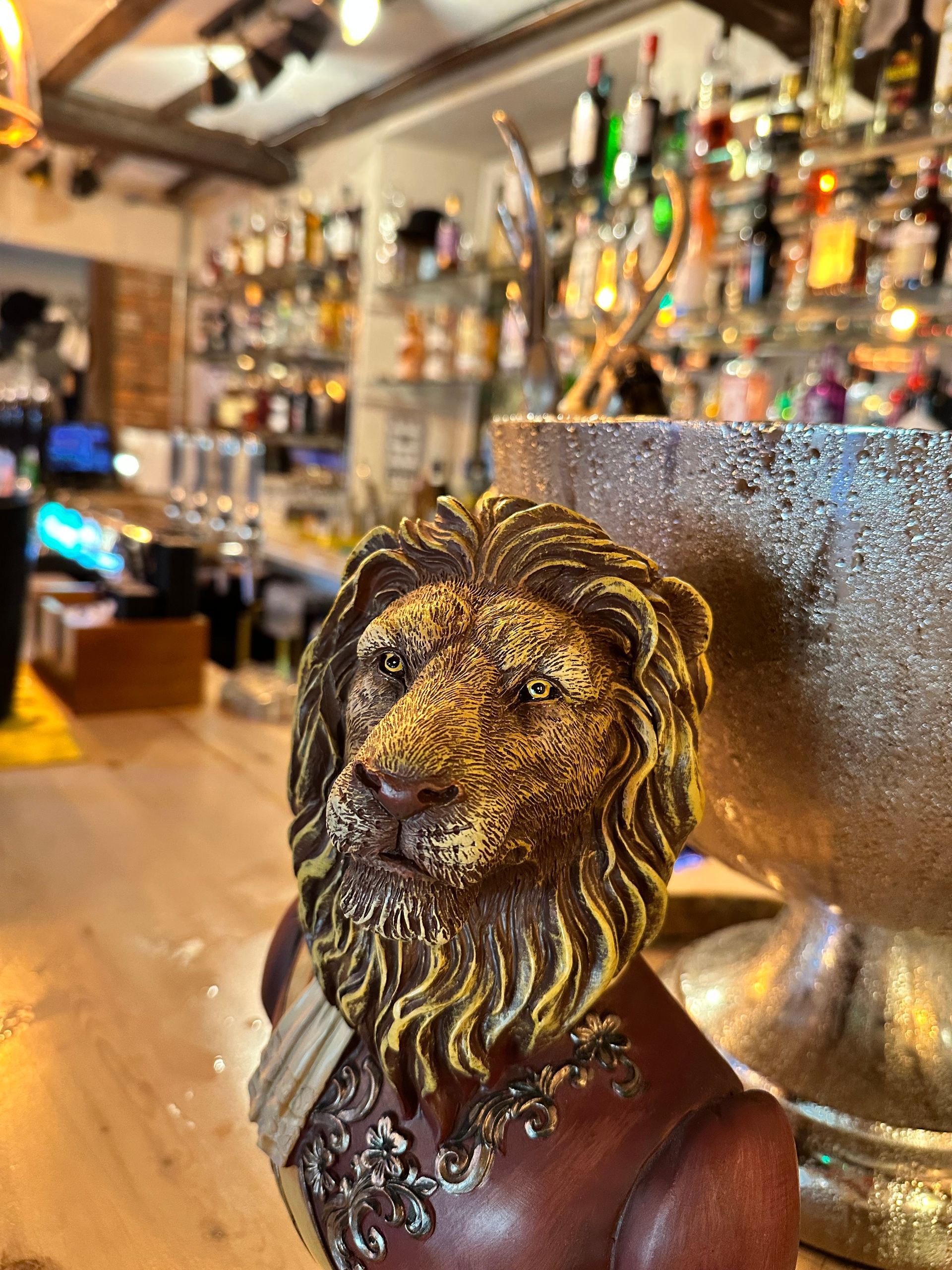 Lion-shaped bar tap handle in a warmly lit pub with shelves of bottles in the background