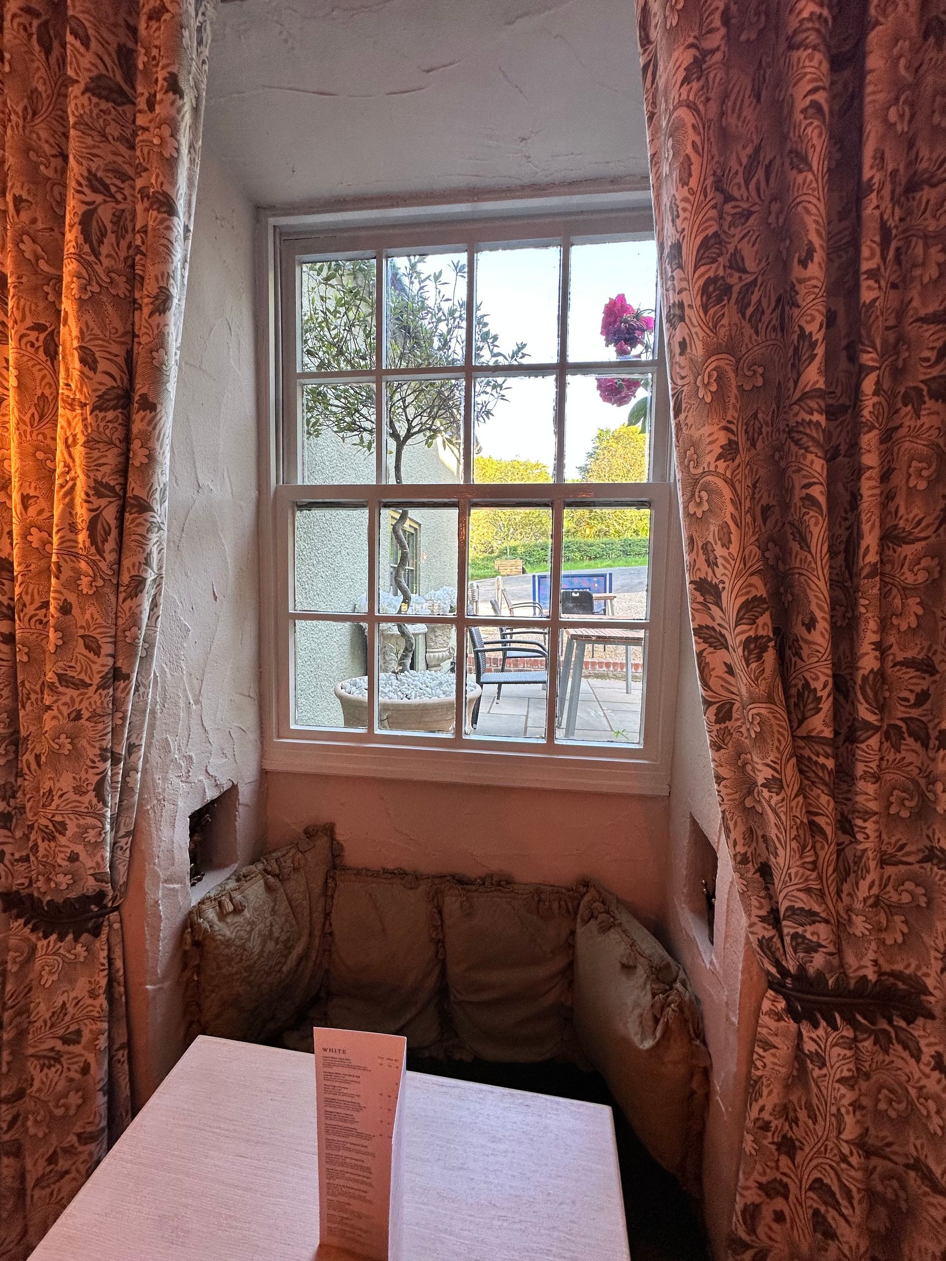 Cozy window nook with patterned curtains, stone walls, and a view of a sunny patio outside