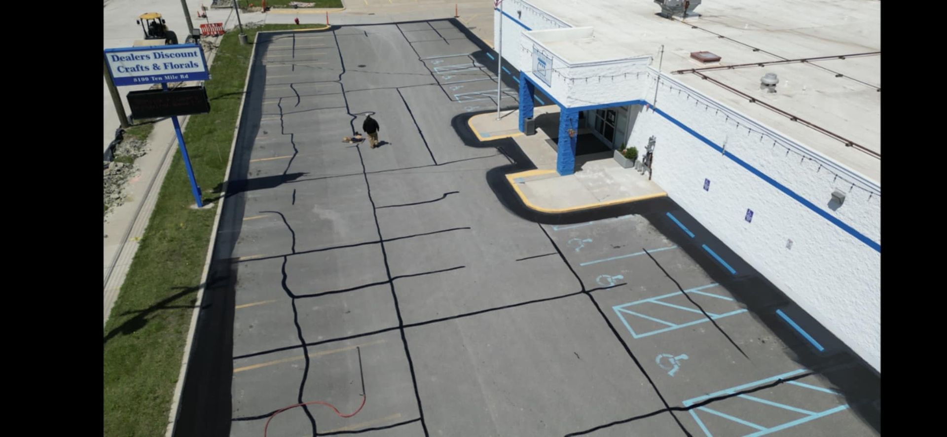 Overhead view of a parking lot and building. A person walks across the lot. Sign in front of a building.