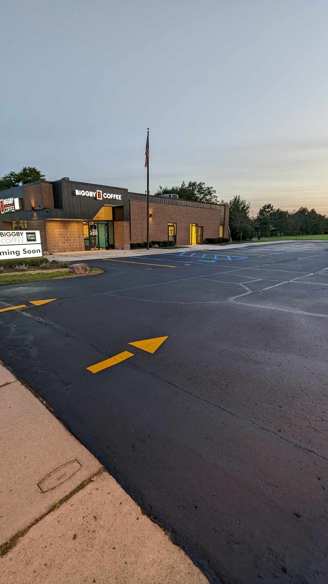 Exterior of a building with parking lot. Yellow arrow points towards the entrance. Twilight sky.