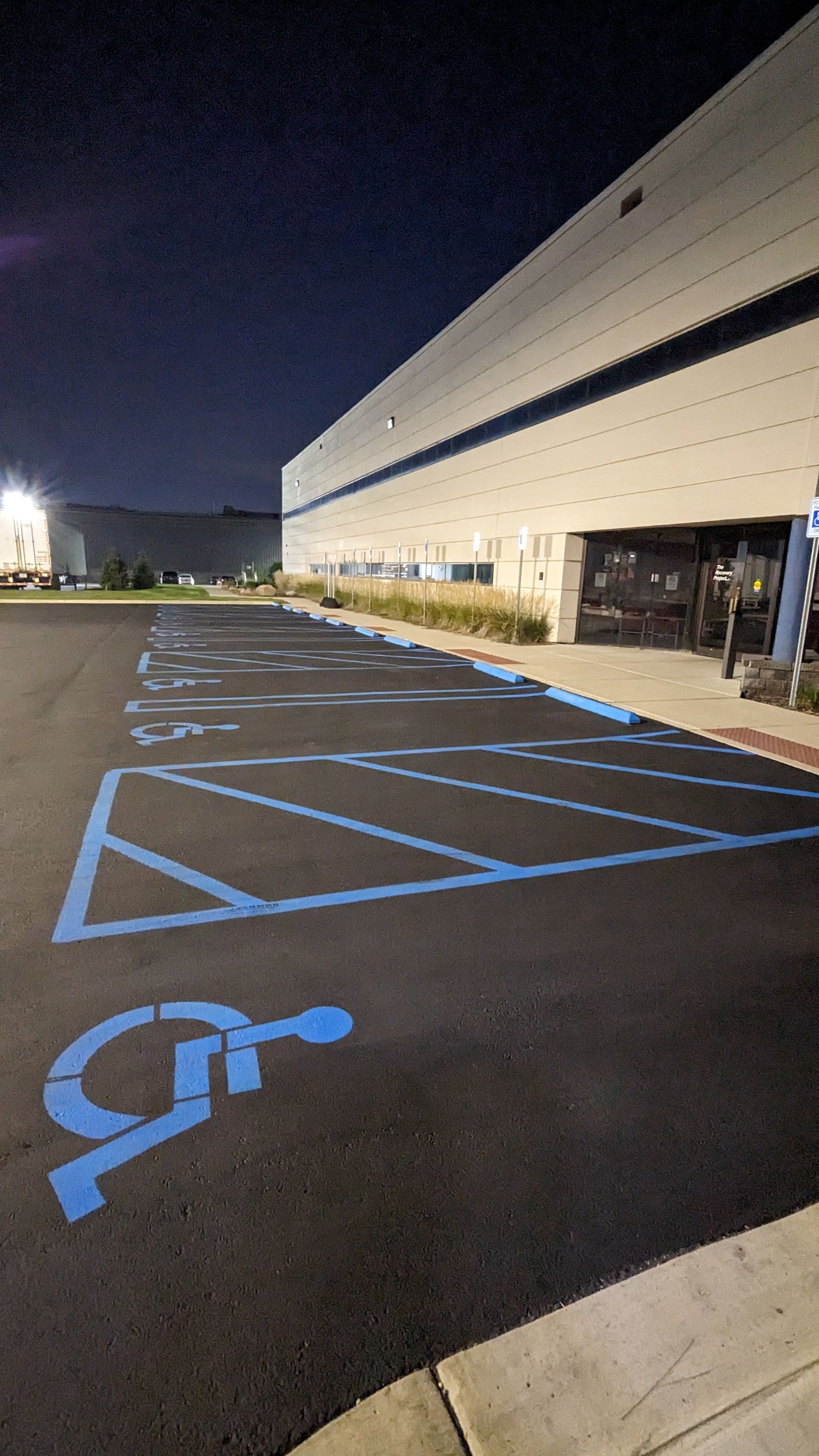 Blue painted handicap parking spaces in front of a large building at night.
