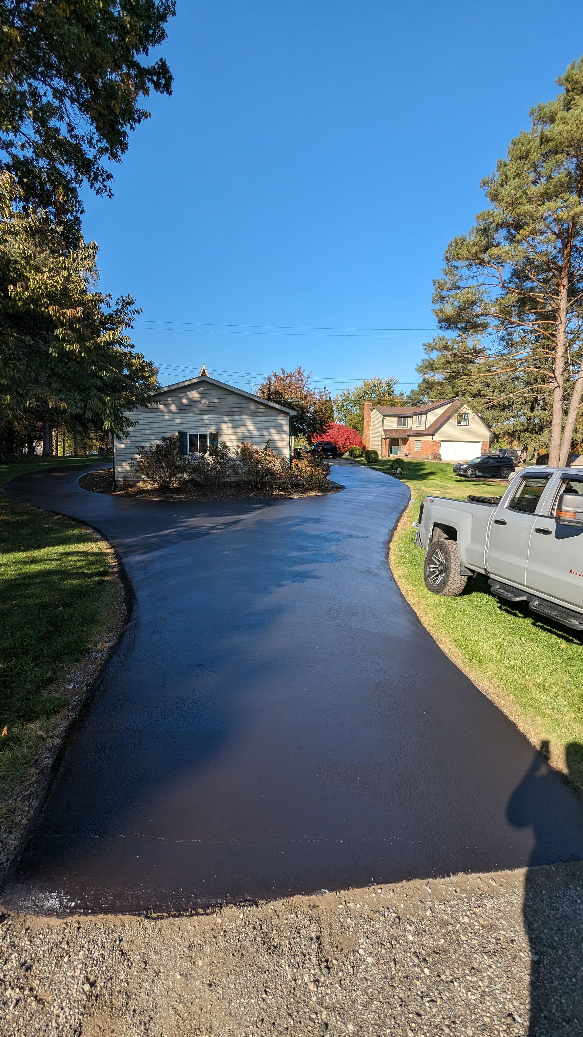 Long, freshly paved driveway curves toward houses and trees under a clear blue sky.