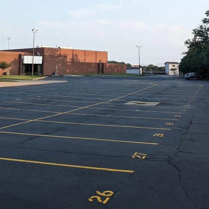 Empty asphalt parking lot with yellow numbered parking spaces in front of a brick building.