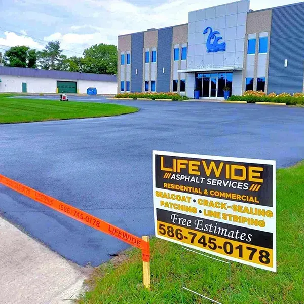 Sign for LifeWide Asphalt Services in front of a building with fresh asphalt.